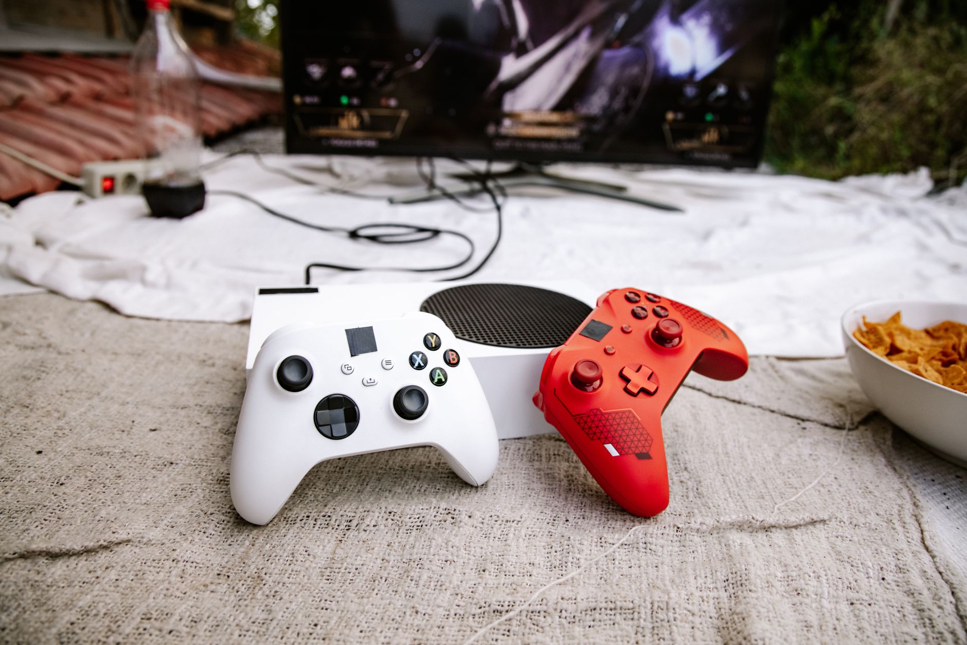 Une console de jeu avec des manettes rouge et blanche installée en extérieur avec un écran de télévision.