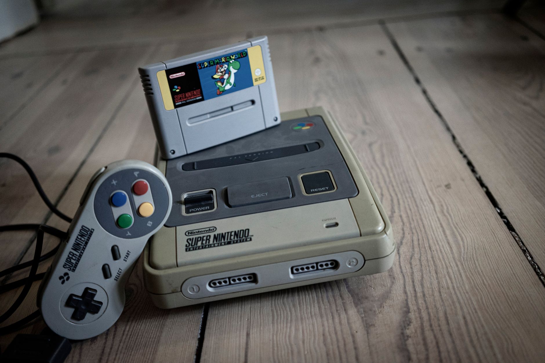 Vue de dessus d'une ancienne console de jeu vidéo avec cassette et manette avec des boutons colorés sur une surface en bois