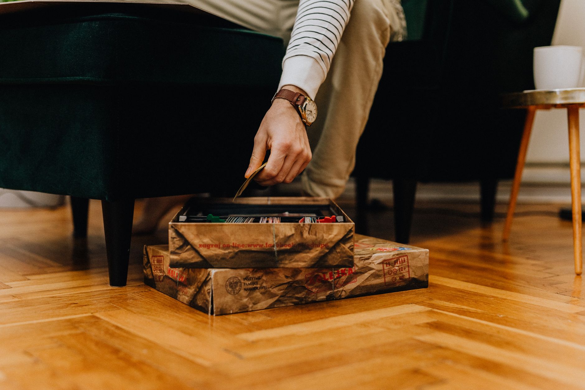 Main plongeant dans une boîte de jeu de société ouverte sur un sol en bois dans un cadre domestique confortable.