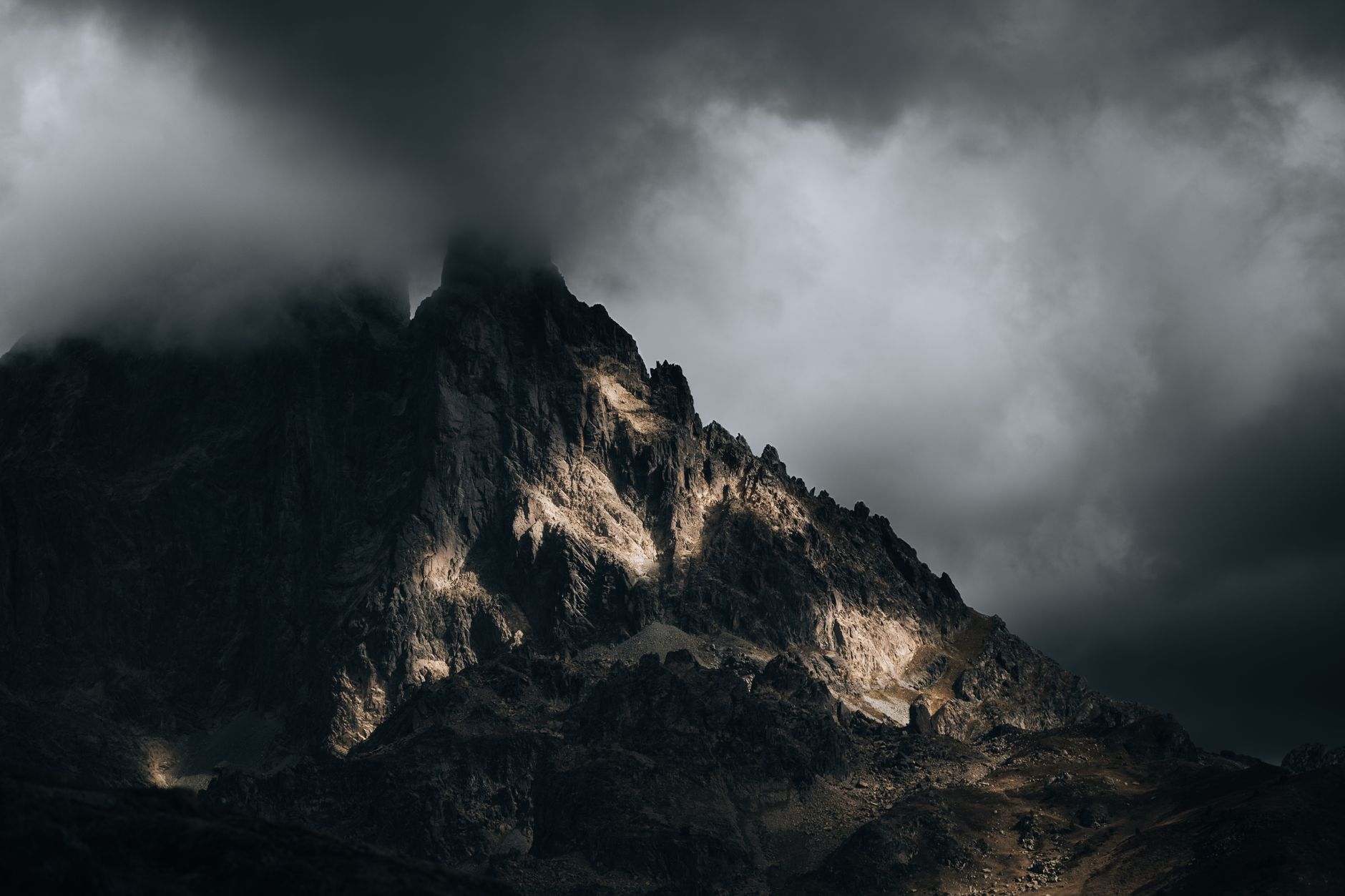 Des nuages sombres enveloppent un sommet de montagne accidenté, créant une scène de paysage dramatique.