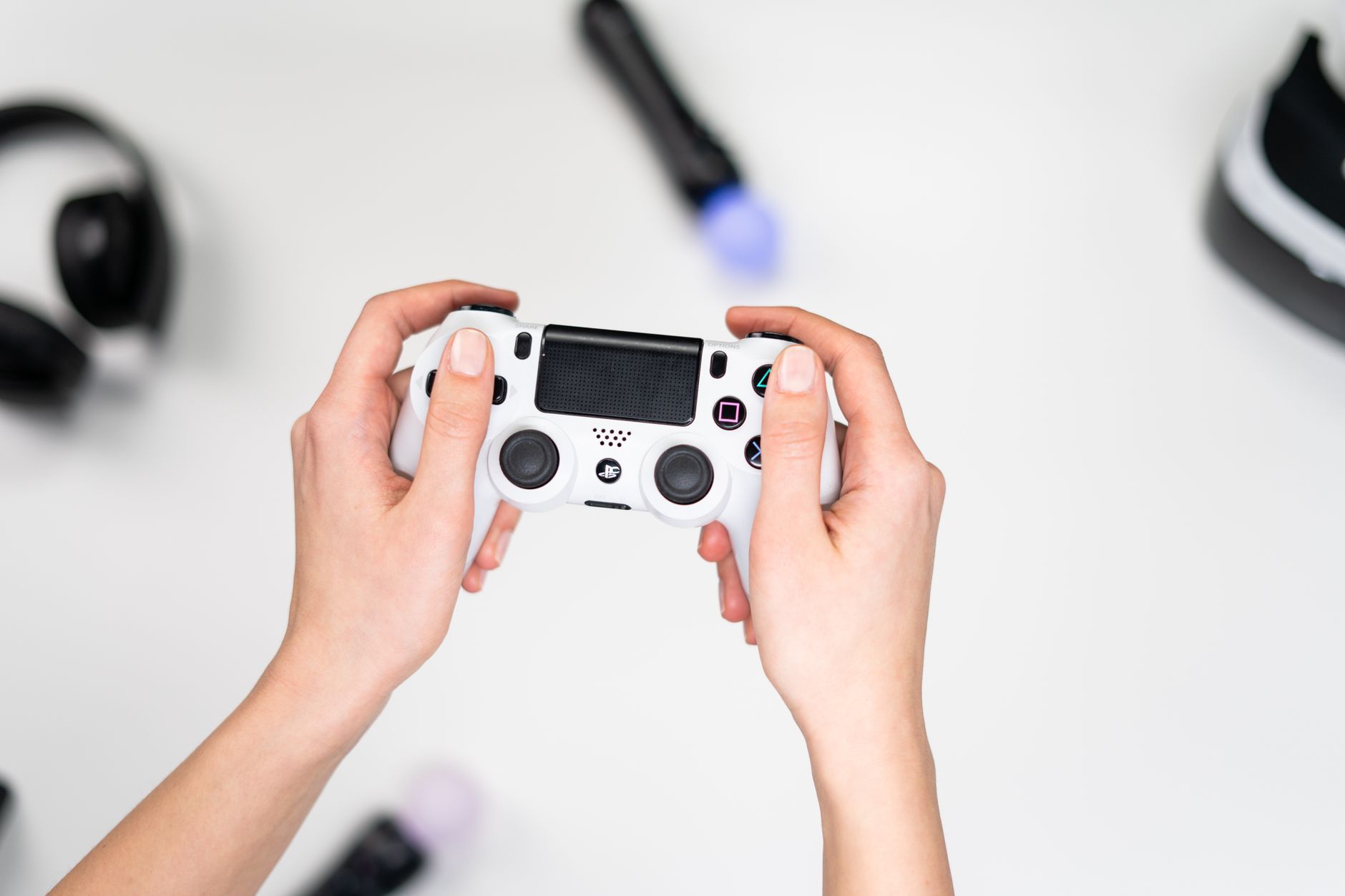 Gros plan sur des mains tenant une manette de jeu blanche sur fond blanc avec des accessoires de jeu à proximité.