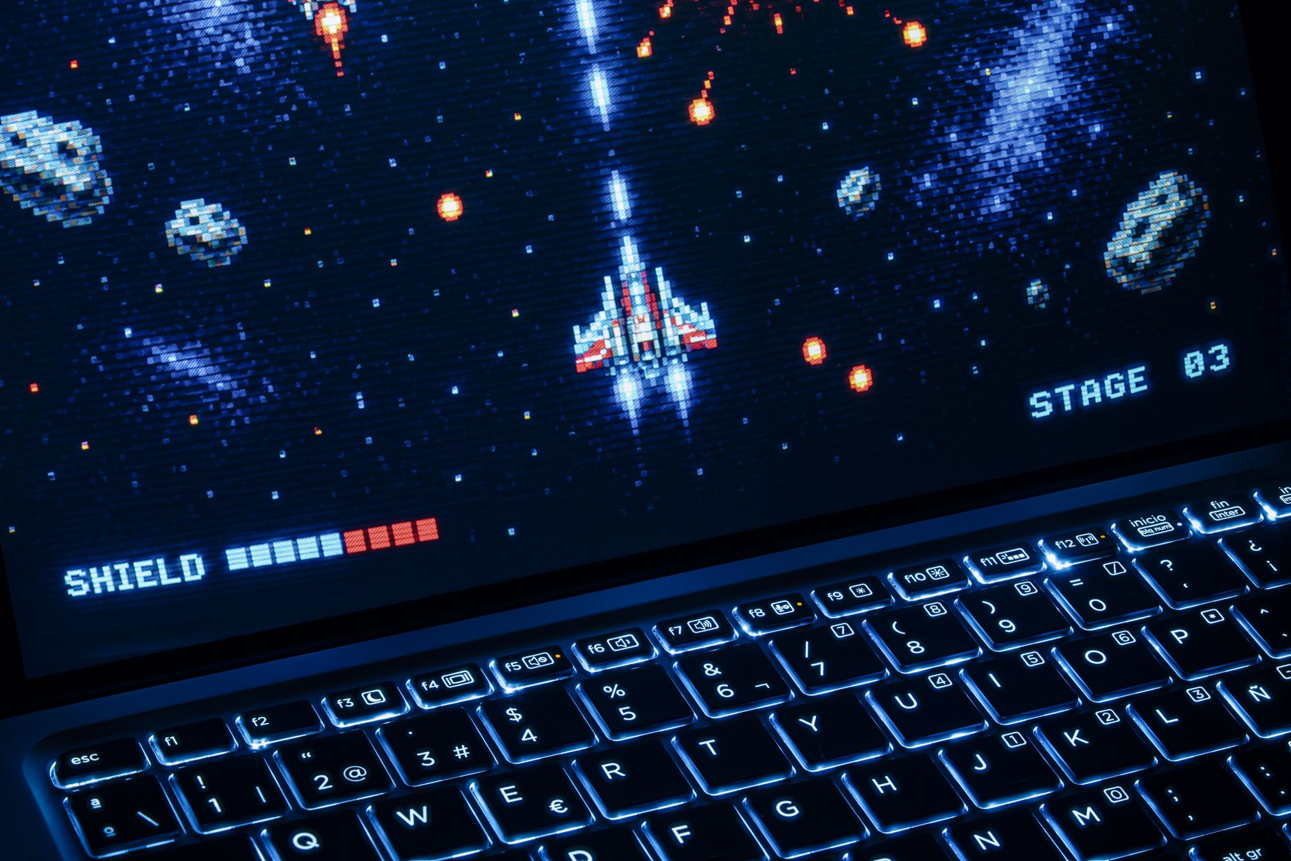 Écran d’ordinateur portable affichant un jeu vidéo d’arcade rétro dans l’espace avec un clavier rétroéclairé.