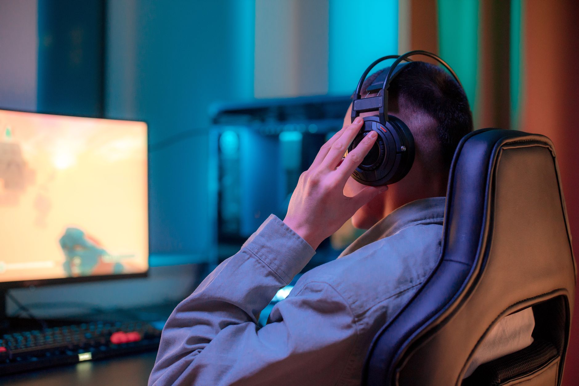 Une personne de dos portant un casque audio devant un écran d’ordinateur dans une pièce éclairée de tons bleus.